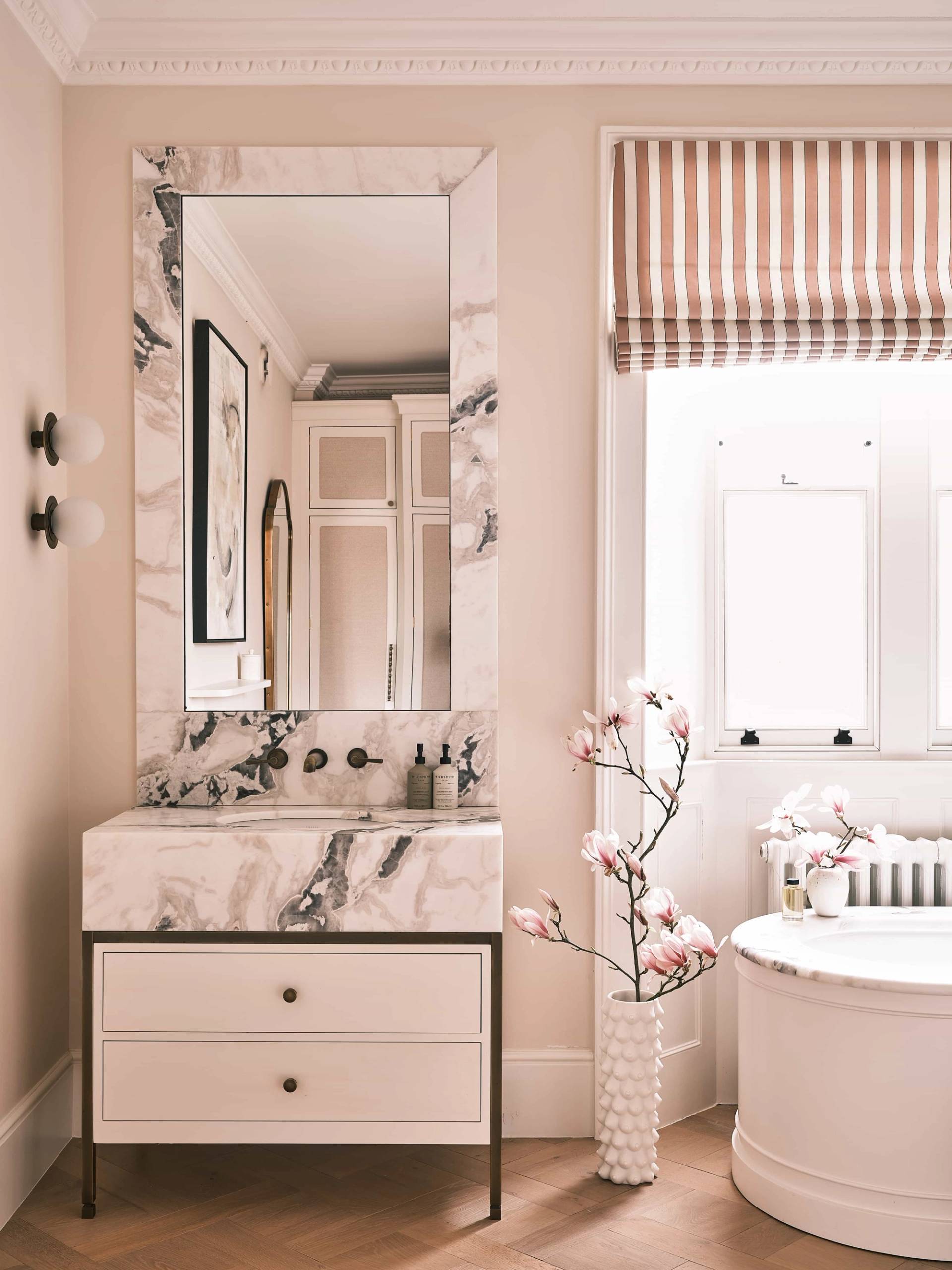 Marble vanity basin detail with dark metal tapware, framed mirror, and pink floral decorations, Love Locations OX7.