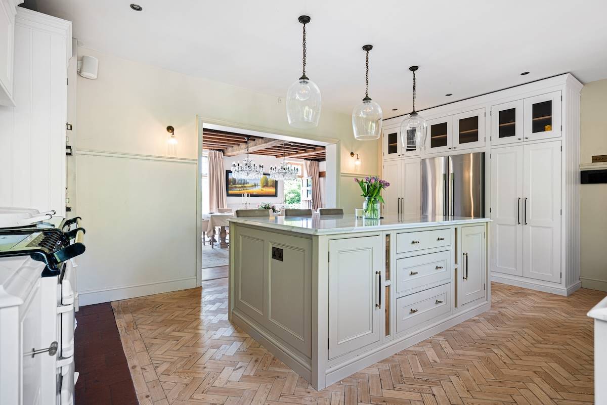 Sleek kitchen island with light green shaker cabinets, marble countertops, and pendant light fixtures, Love Locations RH13.