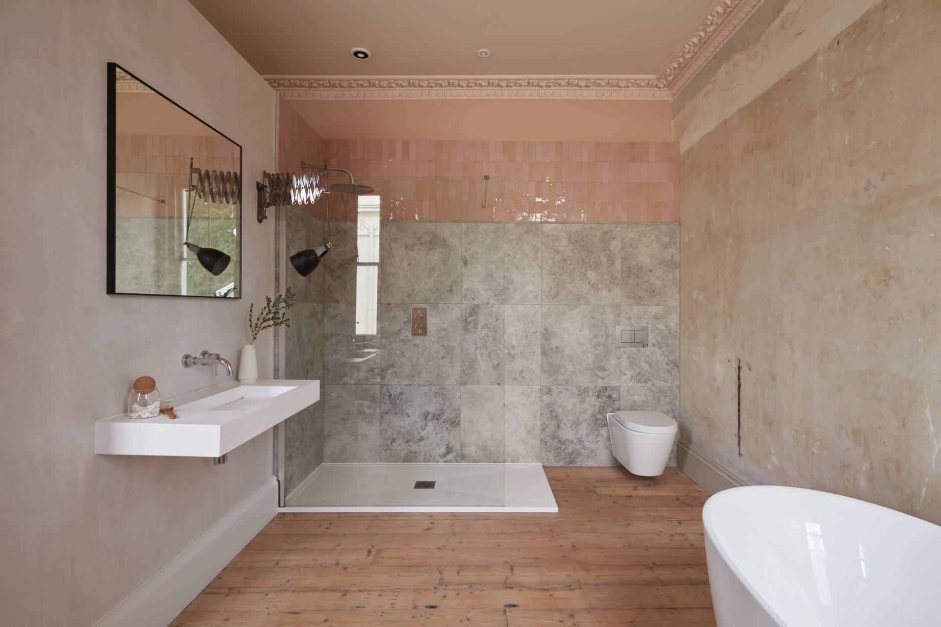 Walk-in shower enclosure with grey stone tiles, brass shower fixtures, and pink tile accents, Love Locations.