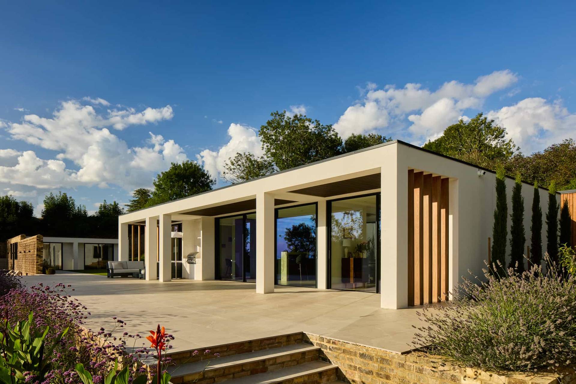 Modern single-storey architectural villa facade opening onto a stone terrace and manicured lawn in Surrey, ideal for automotive campaigns via Love Locations KT22.