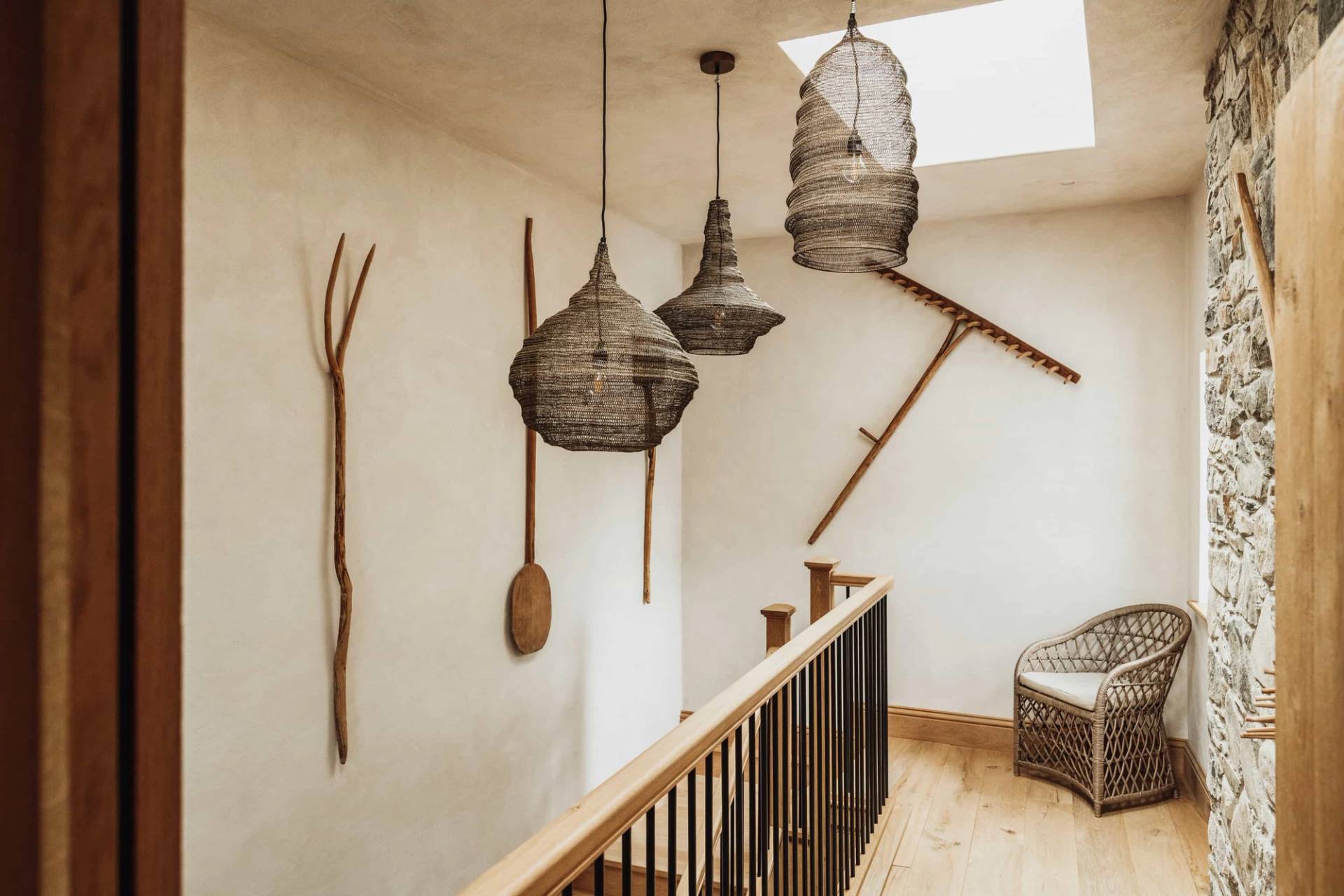 Mezzanine stairwell and landing area in a luxury farmhouse in Castleblayney County Monaghan Ireland by Love Locations, displaying woven pendant lights and rustic wooden paddles on neutral walls.
