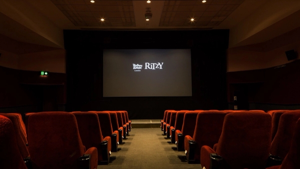 Symmetrical view down the central aisle toward the illuminated projection screen in The Ritzy Screen 2 film location in Brixton SW2, flanked by plush red velvet seats, available through Love Locations.