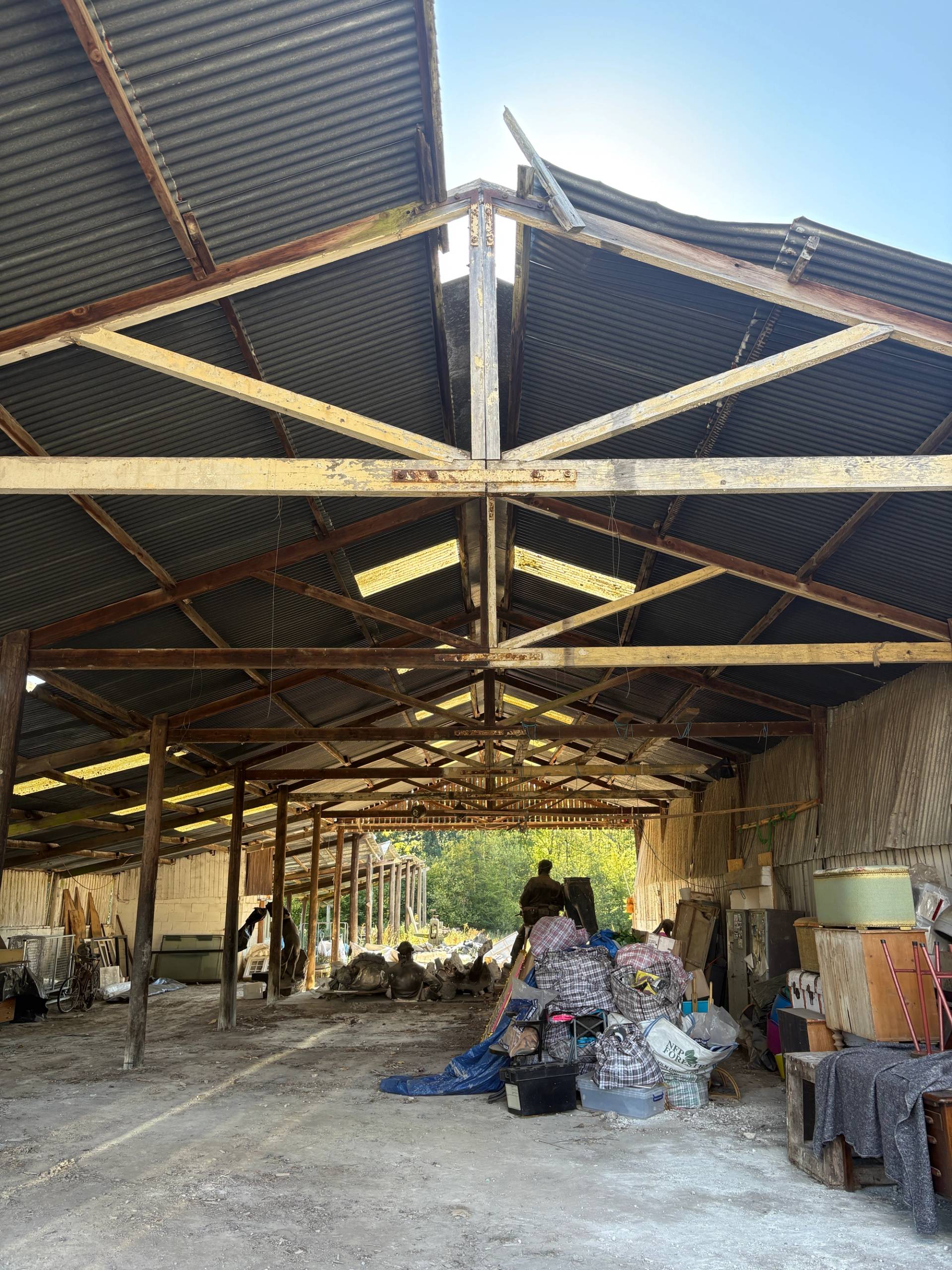 Interior view of a large open-ended agricultural barn with exposed roof trusses and concrete floor, Love Locations BN8.