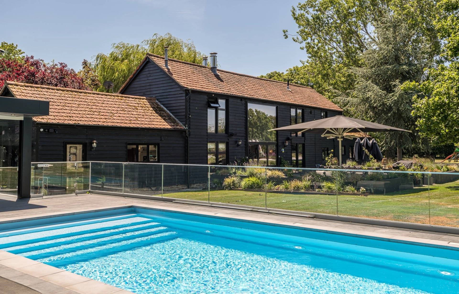 High-end lifestyle location showing a heated outdoor swimming pool in front of an expansive black Essex barn, Love Locations.