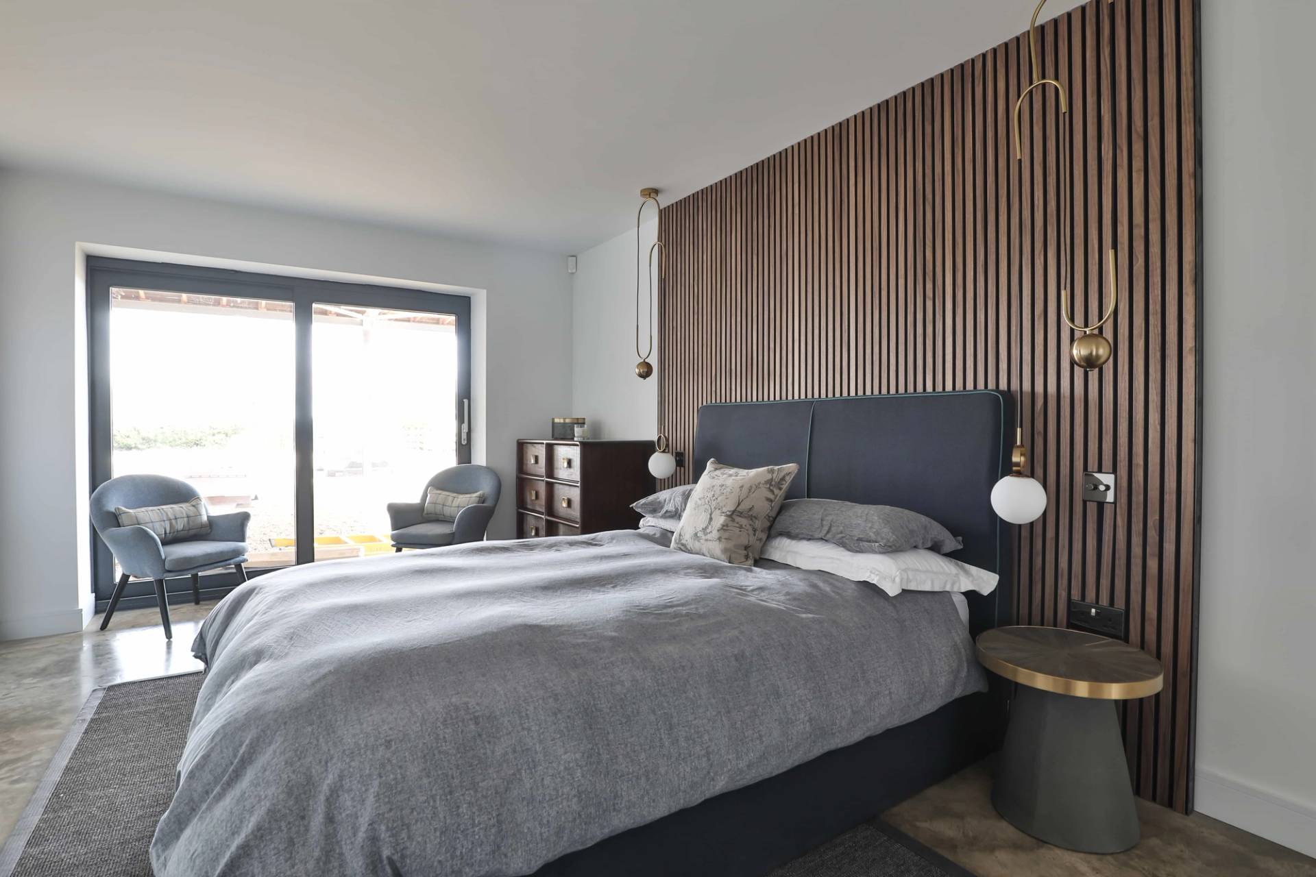 Modern bedroom with slatted wood wall panelling, upholstered bed frame, and sliding glass patio doors, Love Locations CV23.