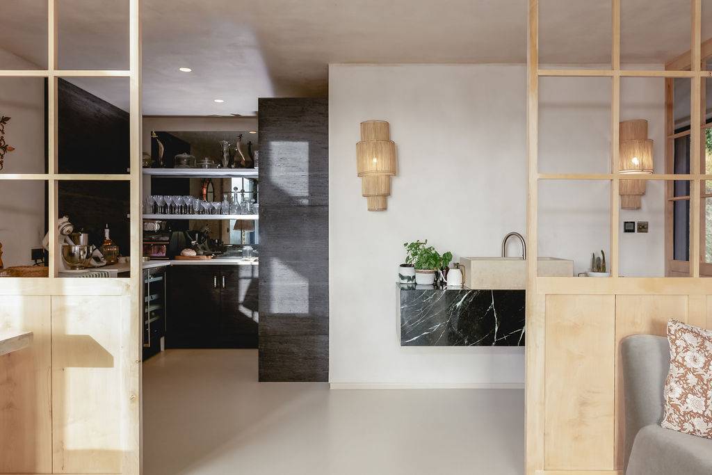 Detail view of microcement partition walls and black marble prep counter set beside framed glass doors, Love Locations GU32.