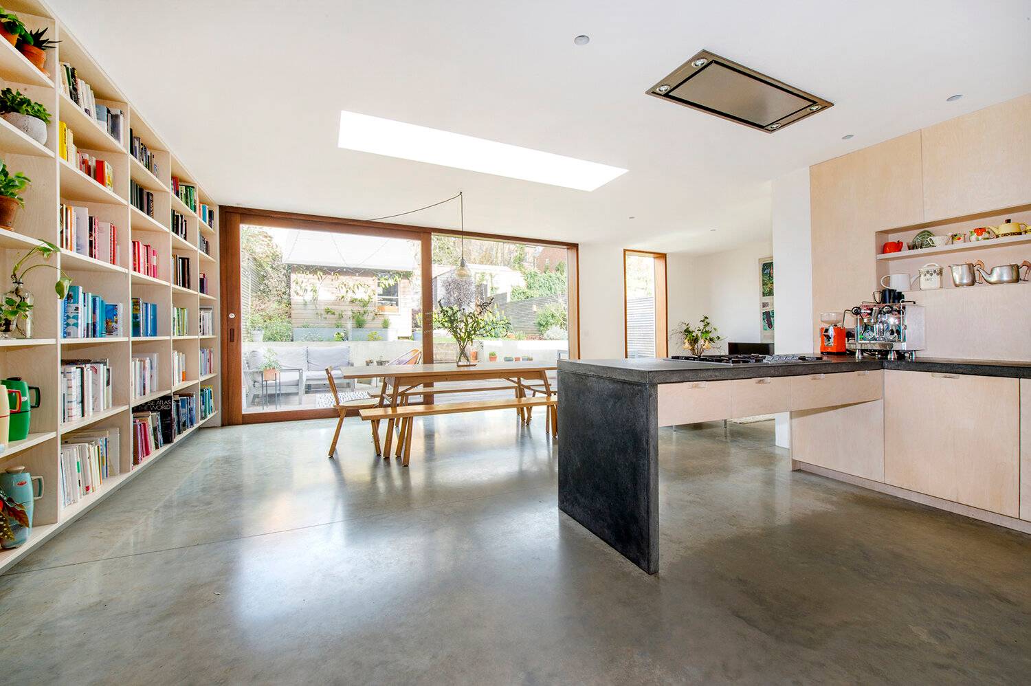 Contemporary kitchen extension shoot location in Forest Hill, SE23 featuring polished concrete floors, long timber dining table, skylights, and garden sliding doors via Love Locations.