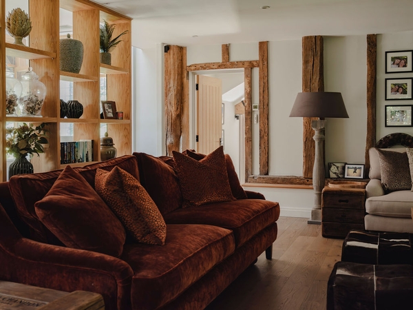 Deep red velvet sofa styled beside bespoke oak shelving and warm table lamps in a converted barn home, Love Locations RG9.