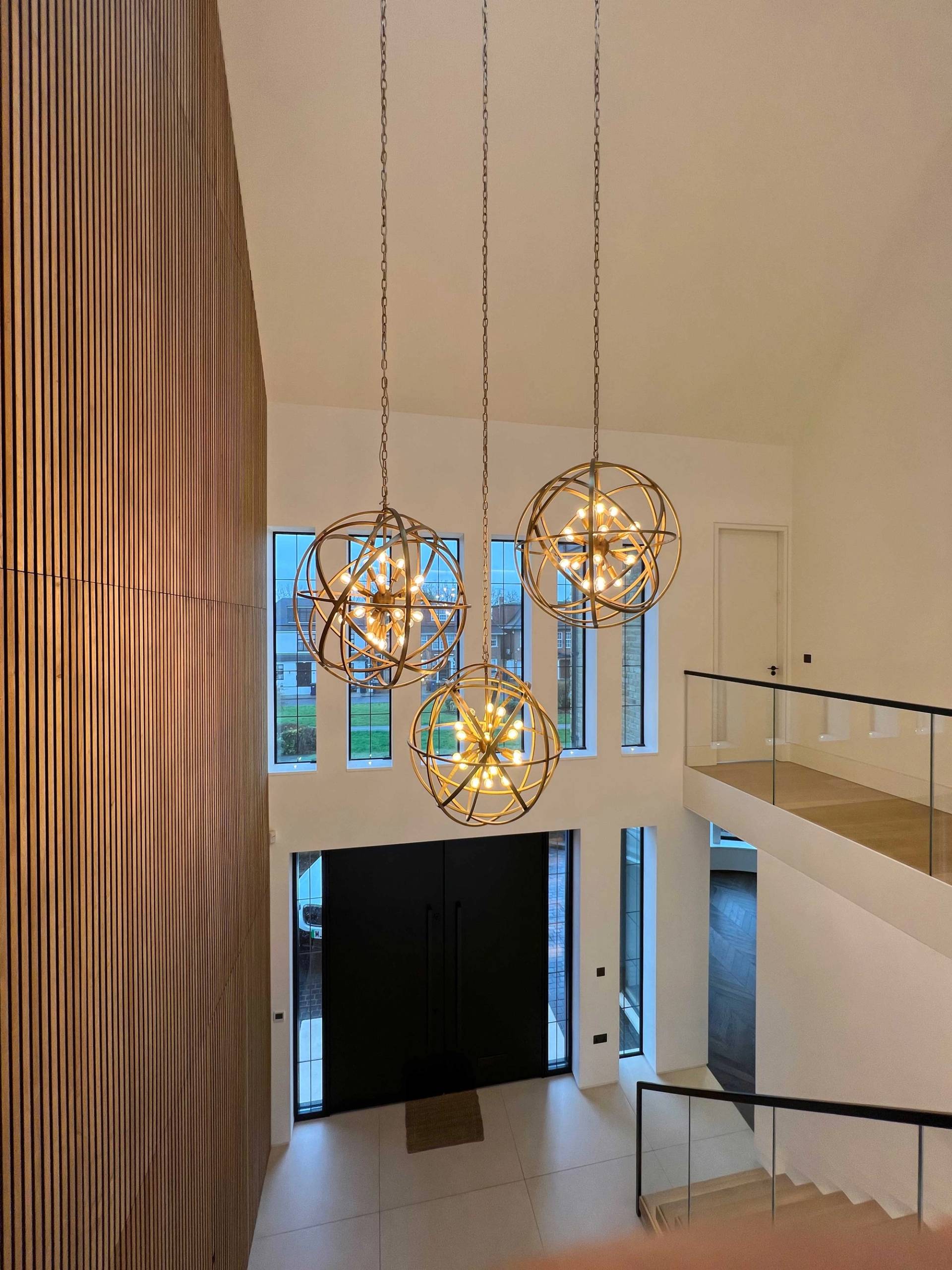 Double-height entrance foyer showcasing cluster brass globe pendant lights and a floating staircase landing, ideal for luxury real estate shoots via Love Locations N3.