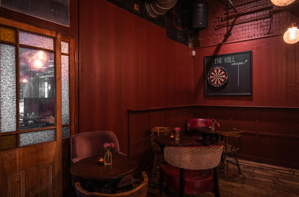Intimate corner booth setup featuring a professional dartboard wall installation, dark leather seating, and retro pub styling, perfect for casual brand campaigns, Love Locations SW16.