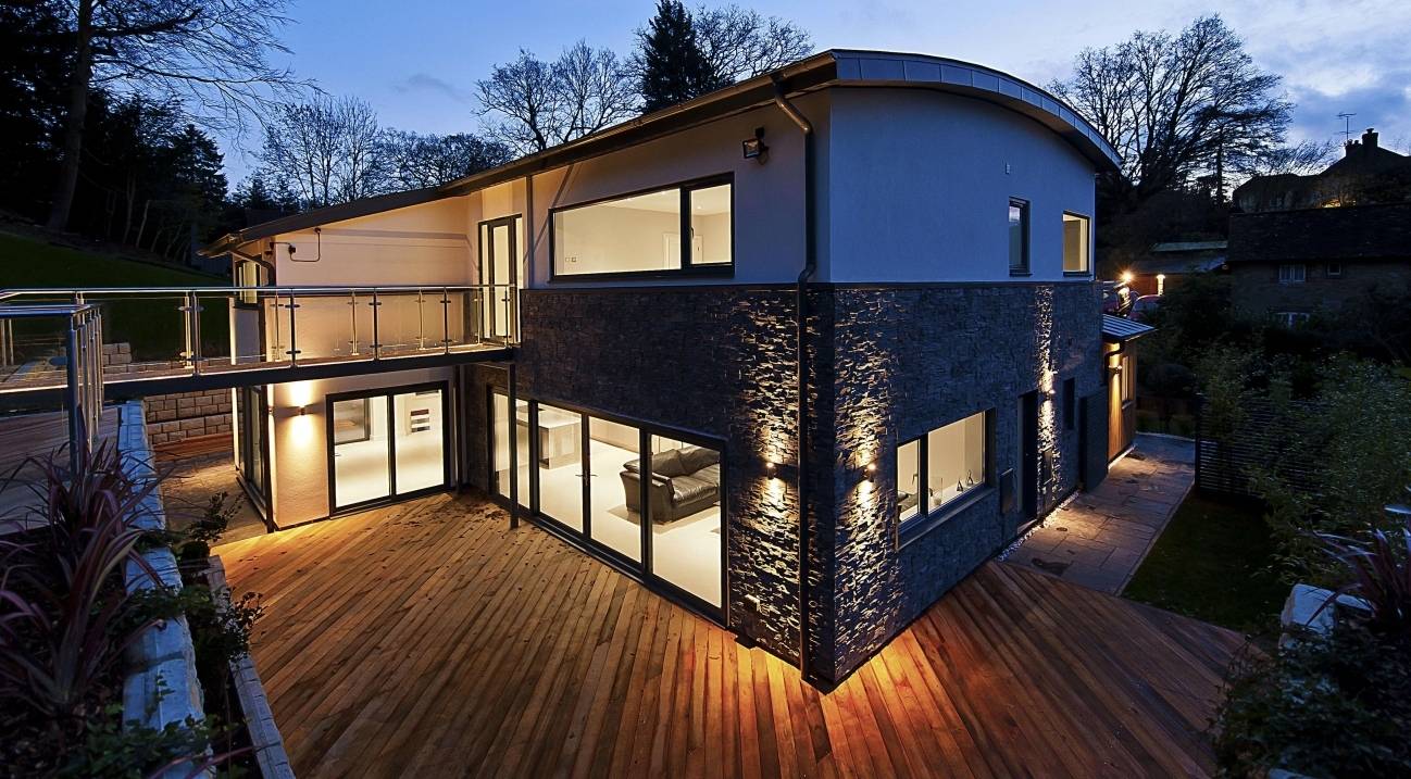 Imposing twilight perspective of a luxury split-face stone cladding house showcasing expansive floor-to-ceiling lit windows, Love Locations.