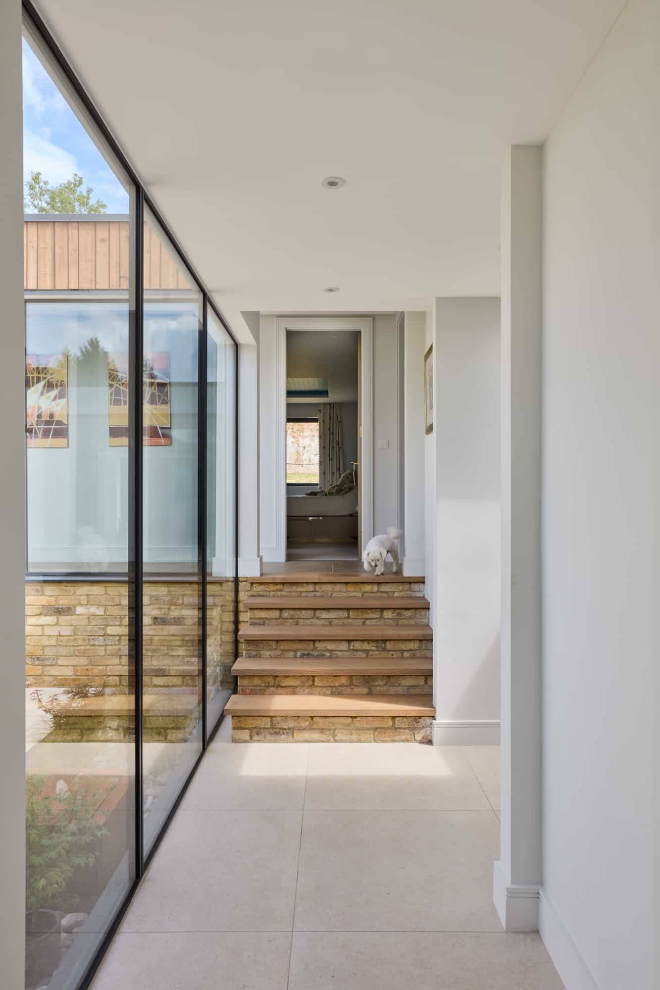 Sunlit internal corridor looking through glass partitions onto a short flight of brick steps and glass courtyard, Love Locations.