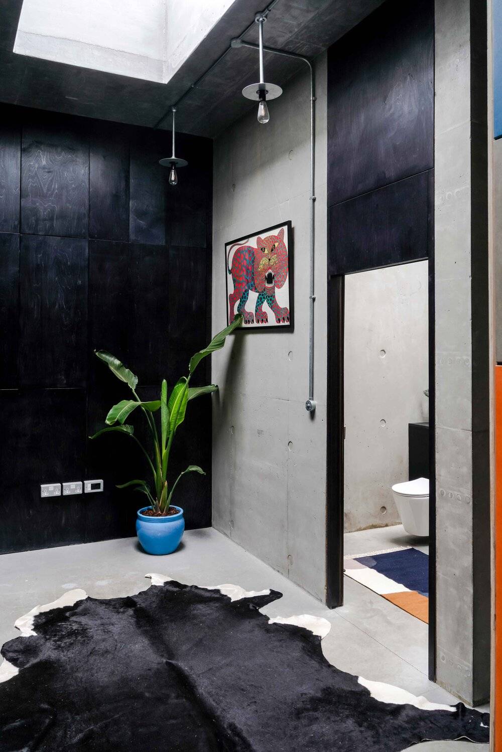 Brutalist bedroom entrance with concrete walls, cowhide rug, black timber panelling, and ensuite doorway, Love Locations BN7.