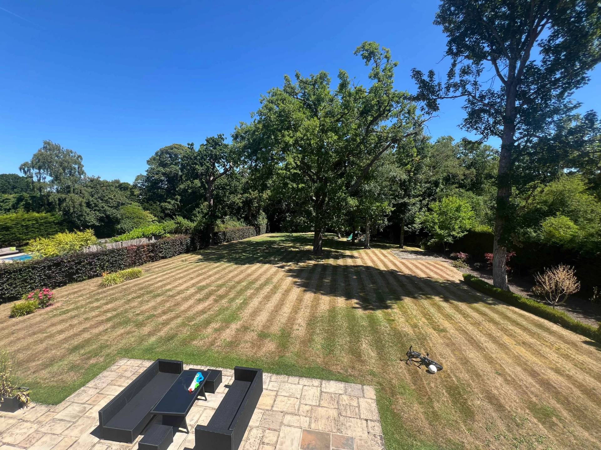 High-angle shot of manicured lawn gardens and stone patio terrace set behind a luxury mansion, Love Locations BR7.