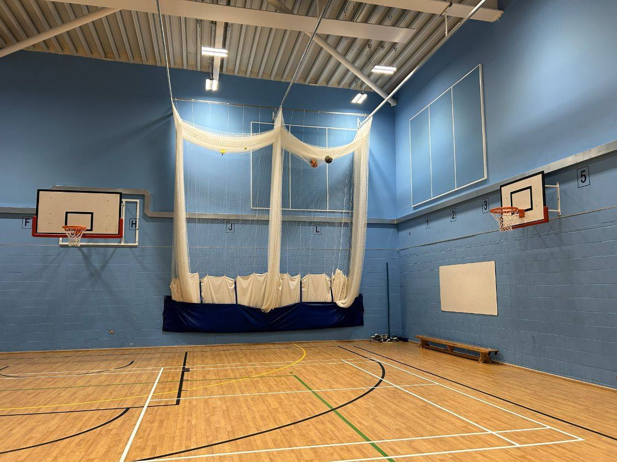 Indoor sports hall photo location featuring retractable cricket netting and blue wall padding via Love Locations.