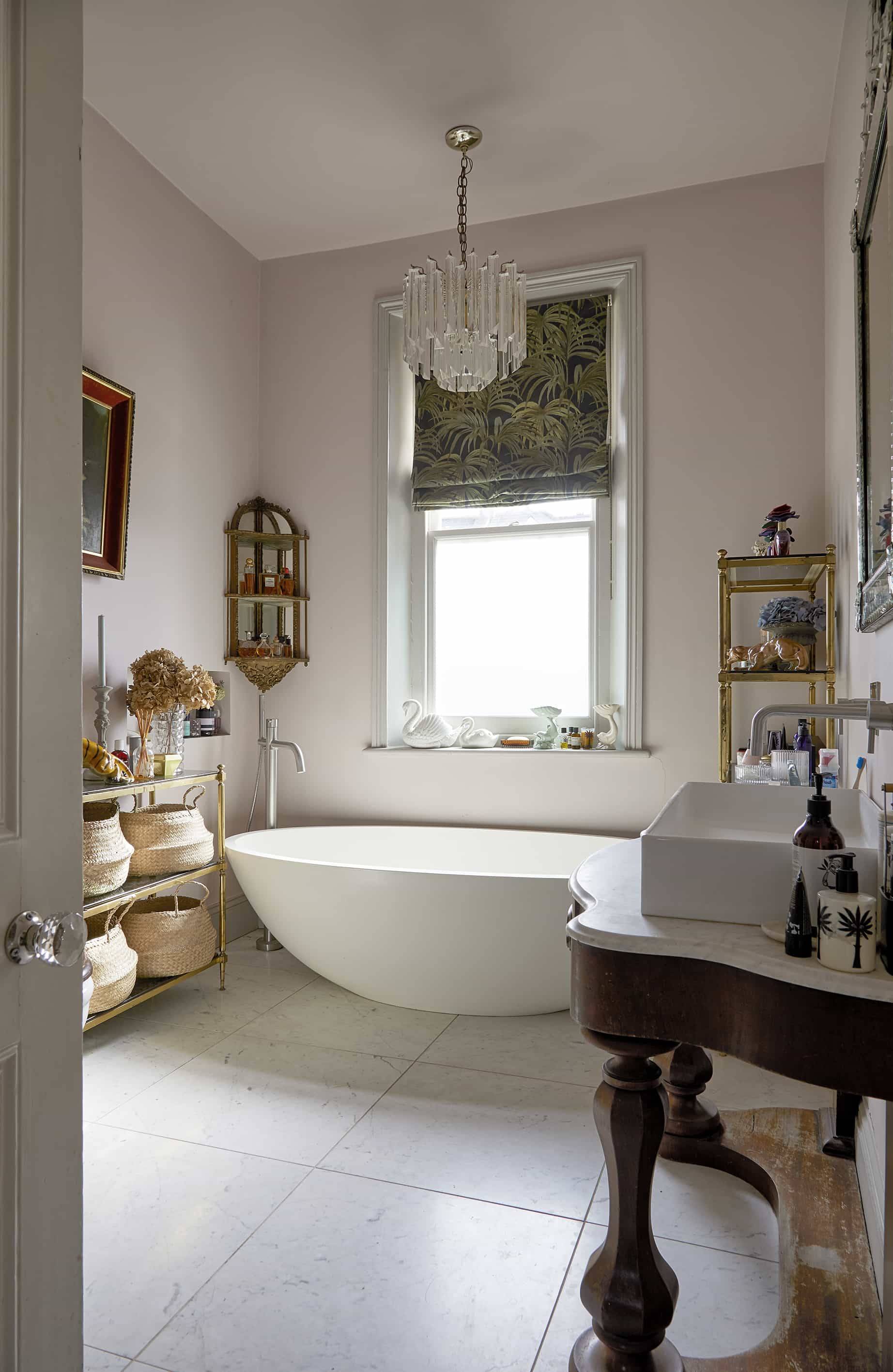 Freestanding oval bathtub set beside a sash window with wooden vanity unit and brass fittings, Love Locations N16.