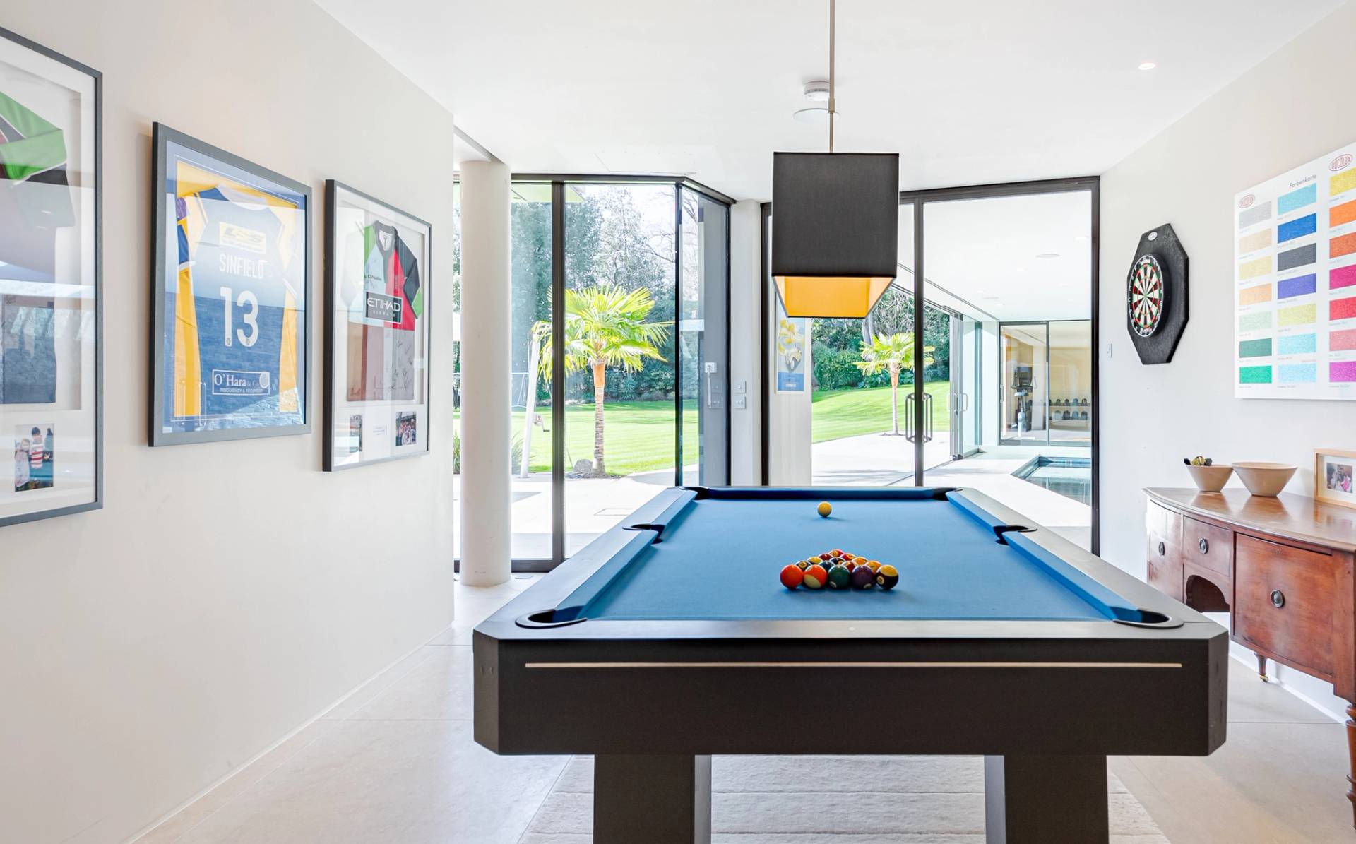 Private games room featuring a modern blue cloth slate pool table, floor-to-ceiling glass windows, and garden views, ideal for lifestyle campaigns, Love Locations KT2.