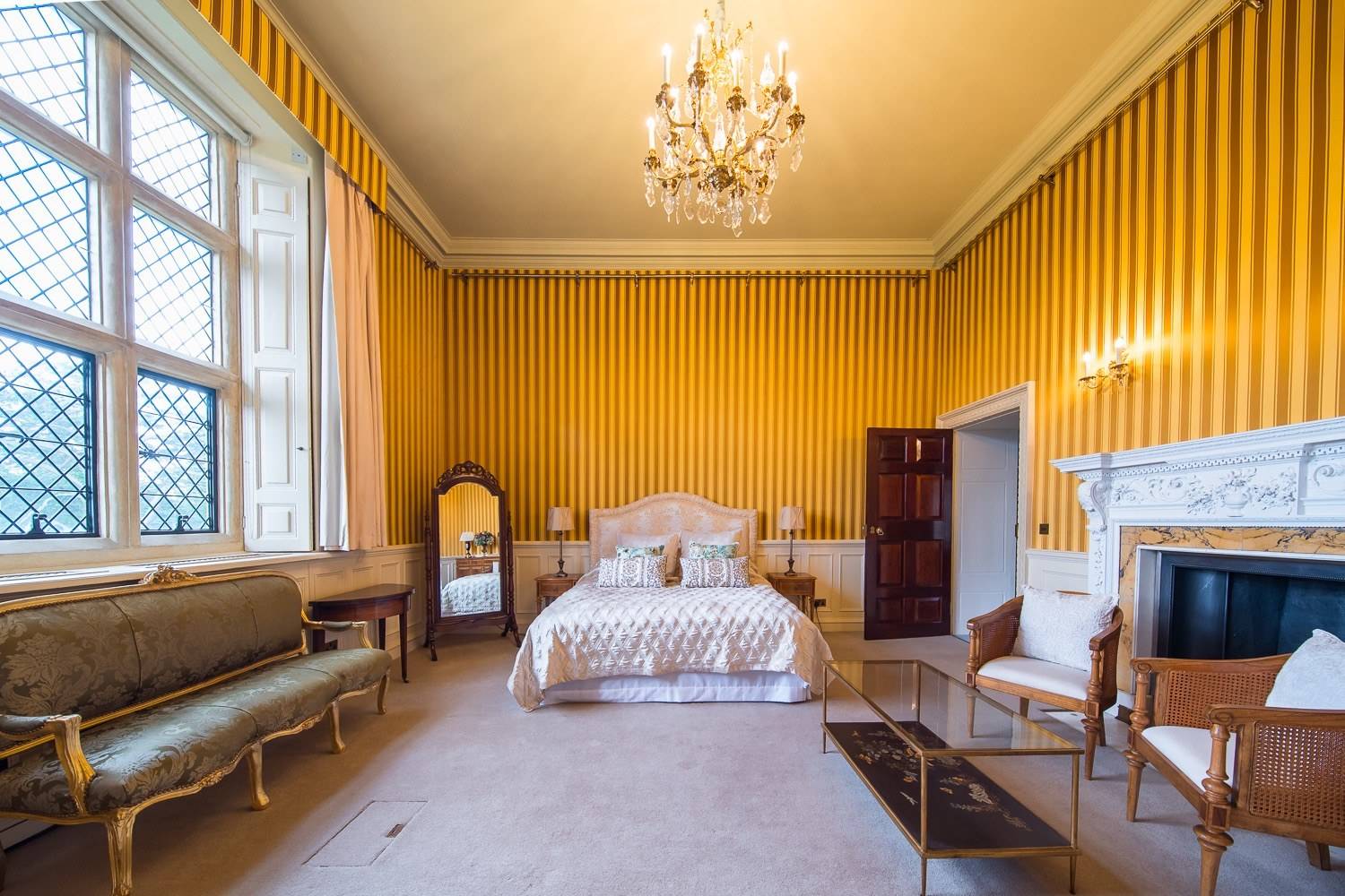 Stately bridal suite bedroom location house in Hertfordshire AL9 from Love Locations, featuring yellow striped wallpaper, padded bed, and period furnishings.
