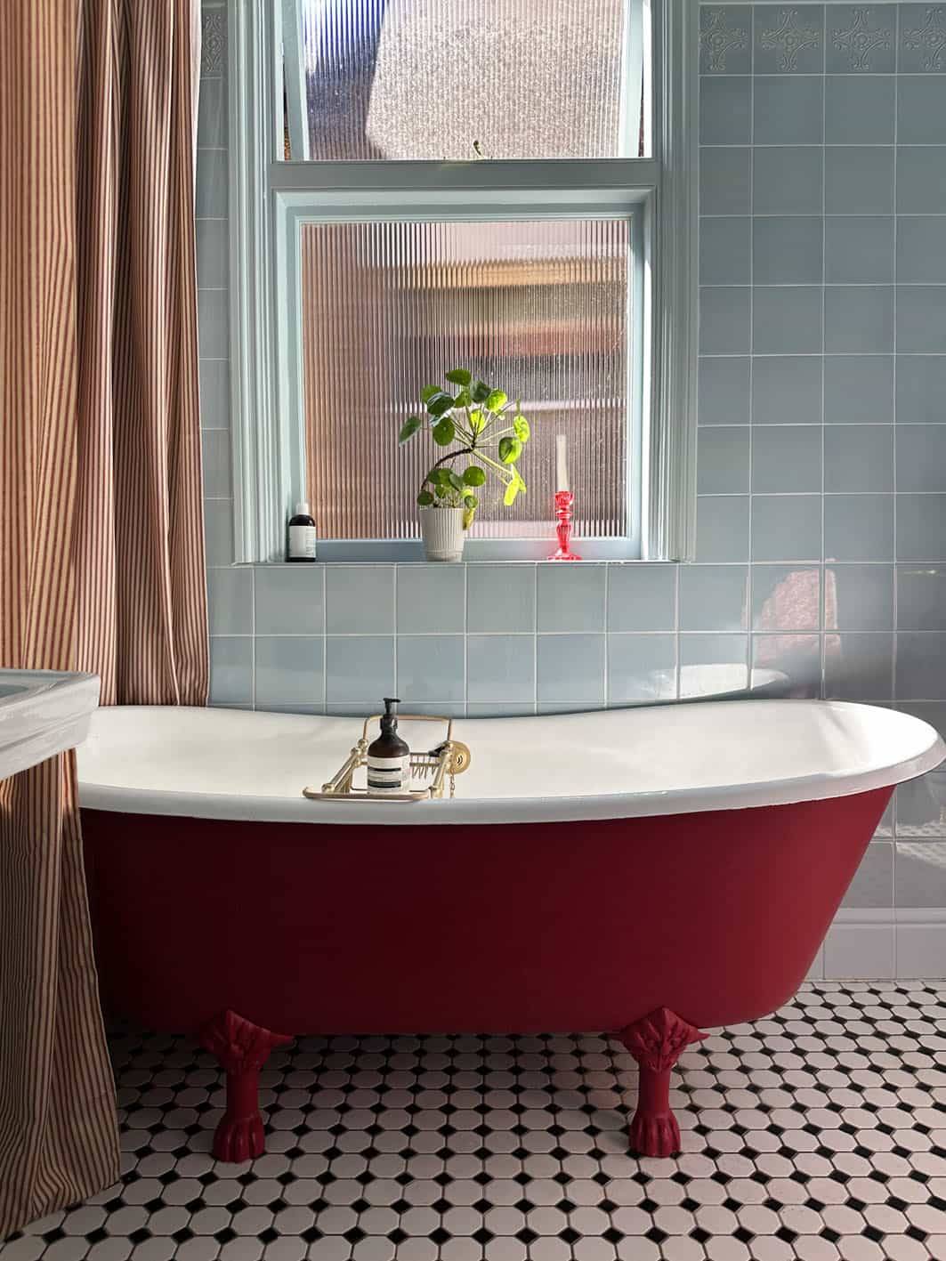 Freestanding red roll-top bath with brass taps set against light blue wall tiles in Palmers Green, Love Locations N13.