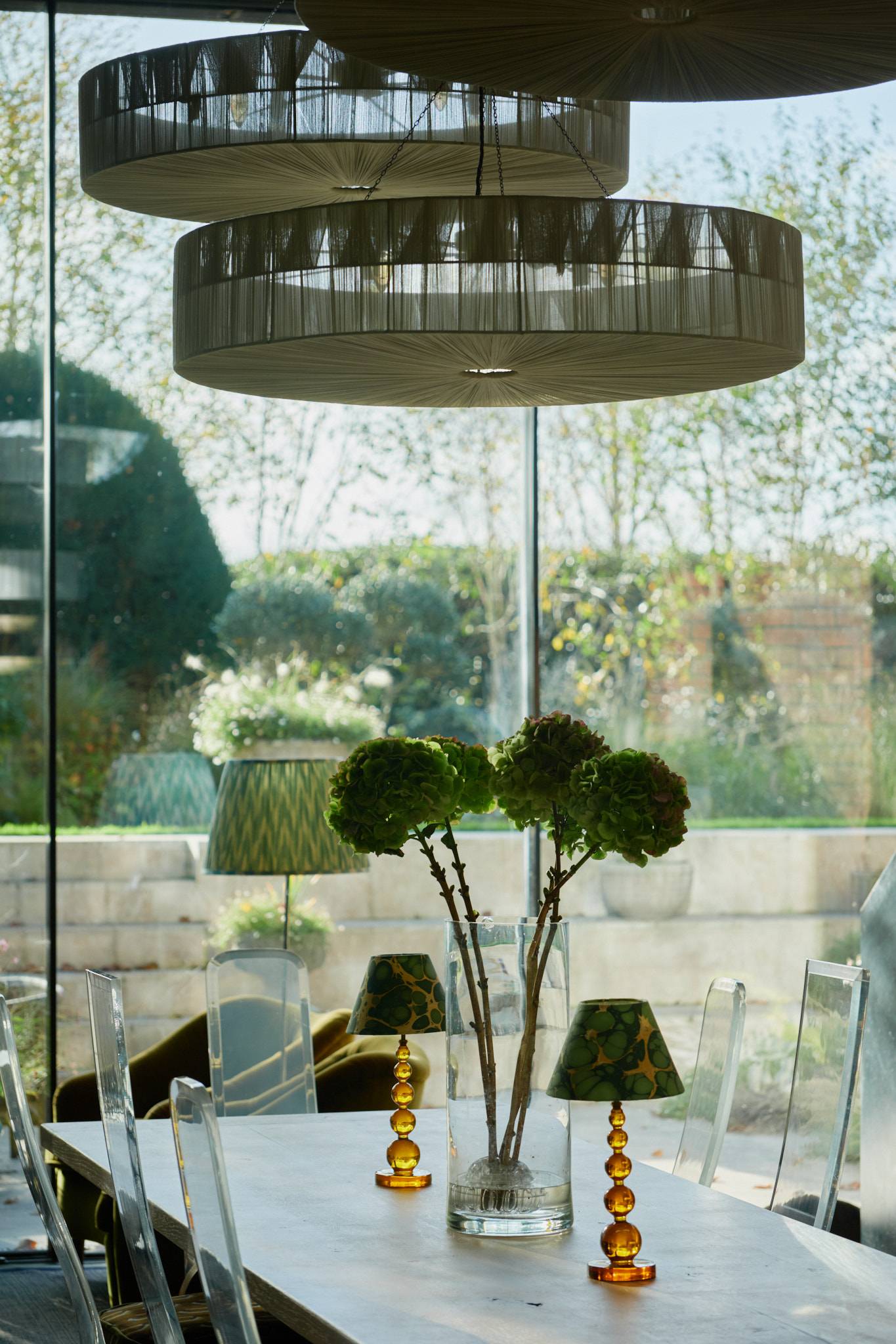 Detailed view of a tall table lamp and green hydrangea floral arrangement framed by full-height window glass, Love Locations SW20.