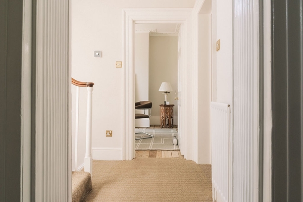 Neutral carpeted hallway landing showing a classic staircase and an open view into rear living spaces, Love Locations SW9.