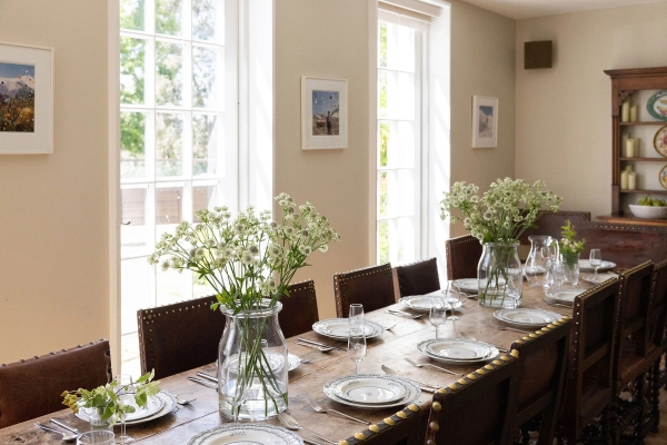 Love Locations boutique dining room location Steyning: Long rustic wooden dining setup dressed with white flowers next to grand sash windows, configured for dinner party scenes in film.
