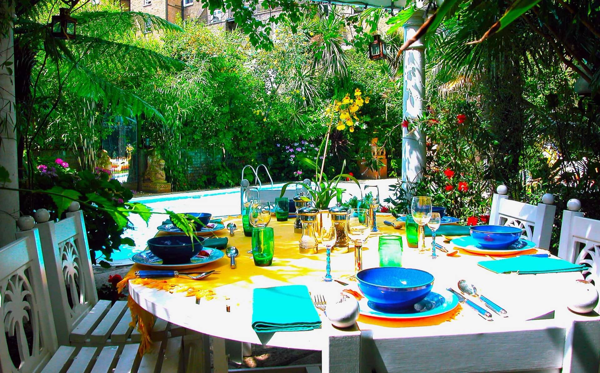 Outdoor dining table set beside a private swimming pool in a tropical garden setting, ideal for summer entertaining campaigns, Love Locations SW5.
