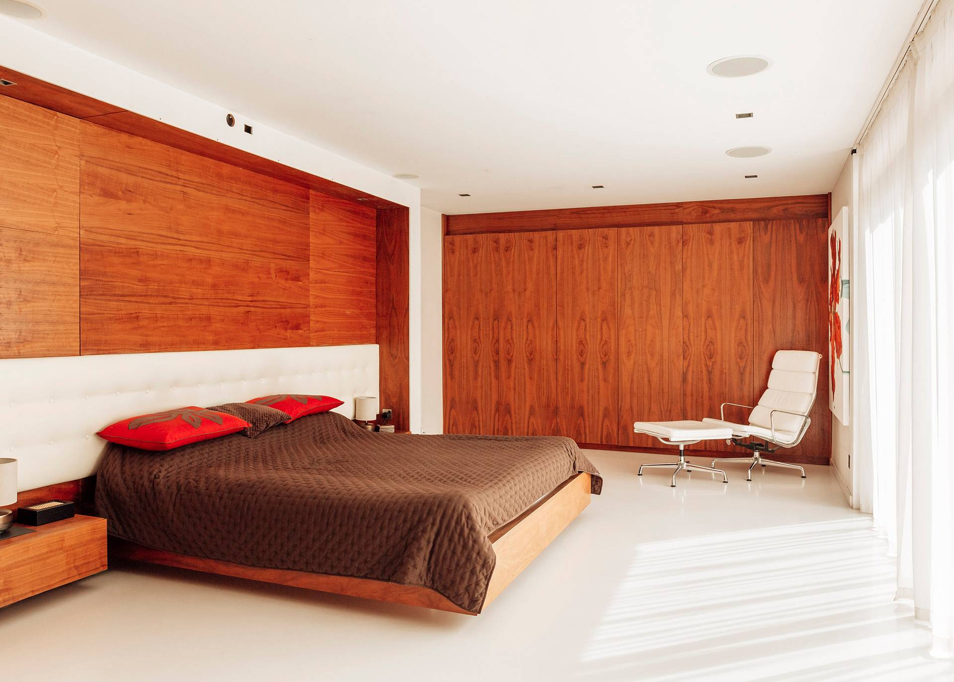 Mid-century master bedroom featuring warm wood wall panelling, a low-profile platform bed, and minimalist seating, Love Locations BR1.
