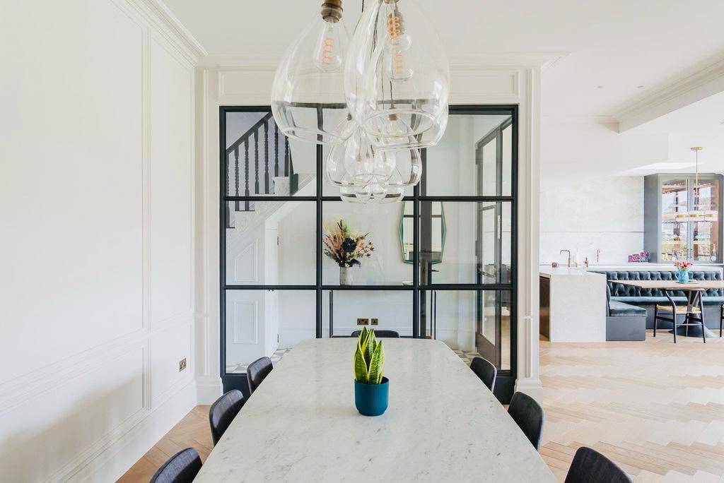 Modern oval marble dining table framed by glass pendant lights and Crittall screen partition, Love Locations TW11.
