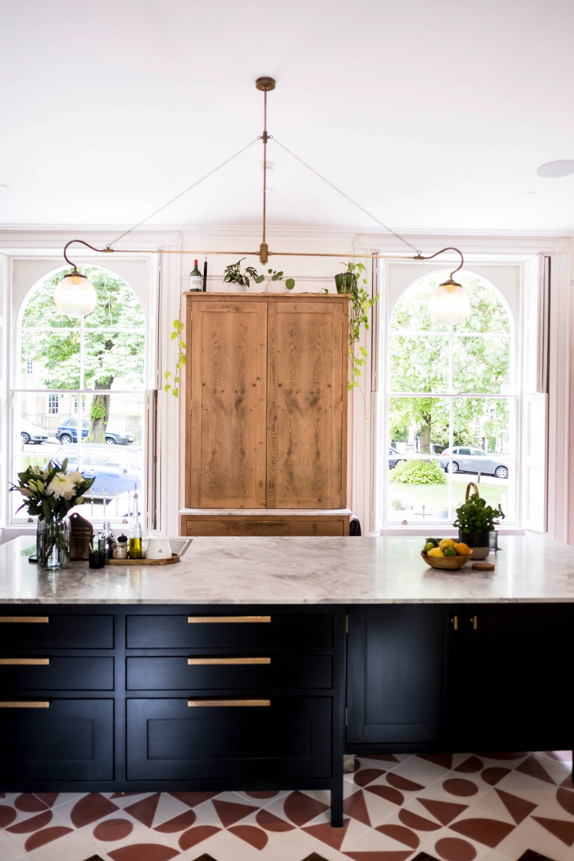 Black kitchen island with marble countertop and oak upper cabinet set against grand sash windows in SE5 via Love Locations.