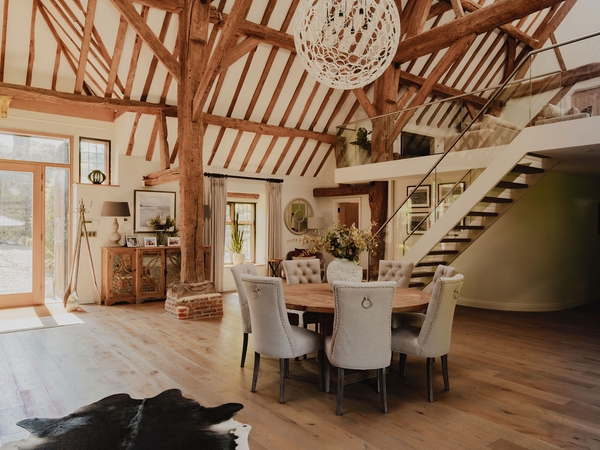 Spacious double-height converted barn room showcasing a round dining table, cowhide rug, and open mezzanine staircase, ideal for luxury brand advertising, Love Locations RG9.