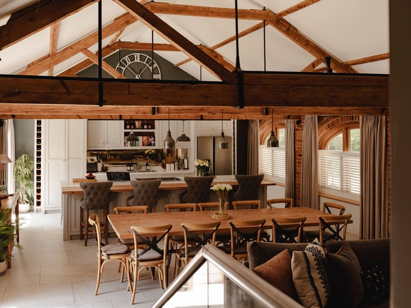 Rustic barn shoot location in Nuffield, RG9 featuring open timber roof trusses, a long wooden dining table, and shaker kitchen island, ideal for country lifestyle campaigns via Love Locations.