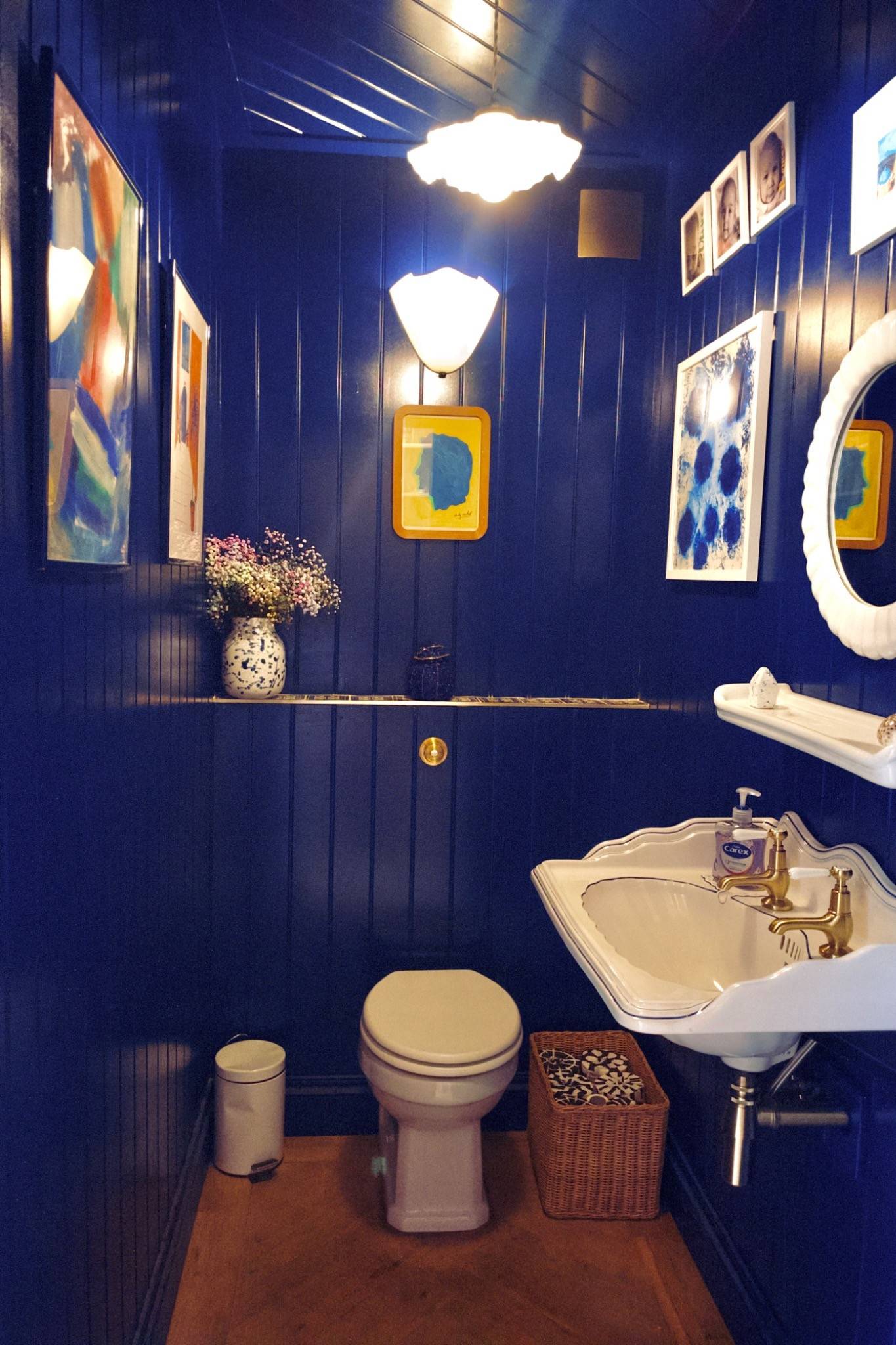 Vibrant deep-blue panelled cloakroom toilet featuring framed nautical wall art and a classic ceramic basin, Love Locations.
