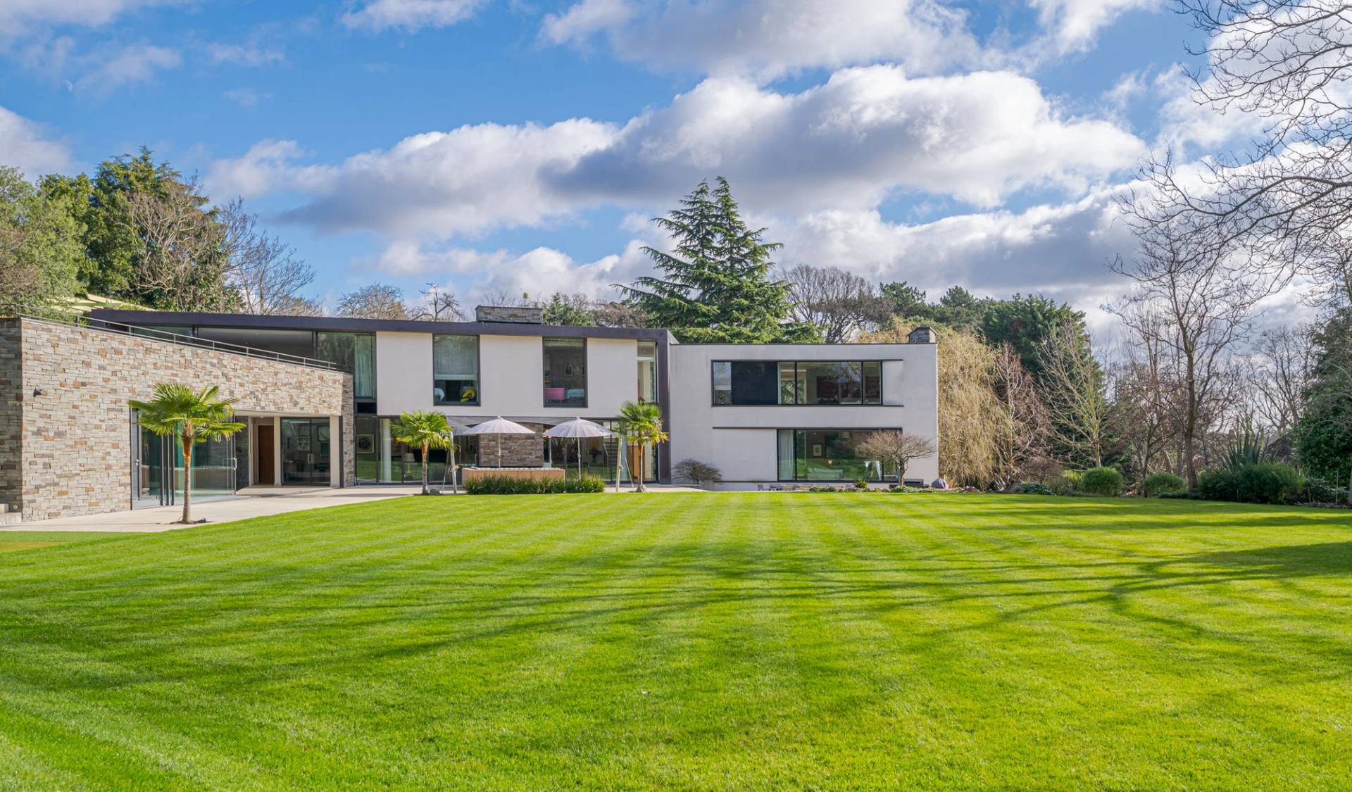 Contemporary mansion rear facade with large glass sliding doors and manicured green lawns in Kingston upon Thames, Love Locations KT2.