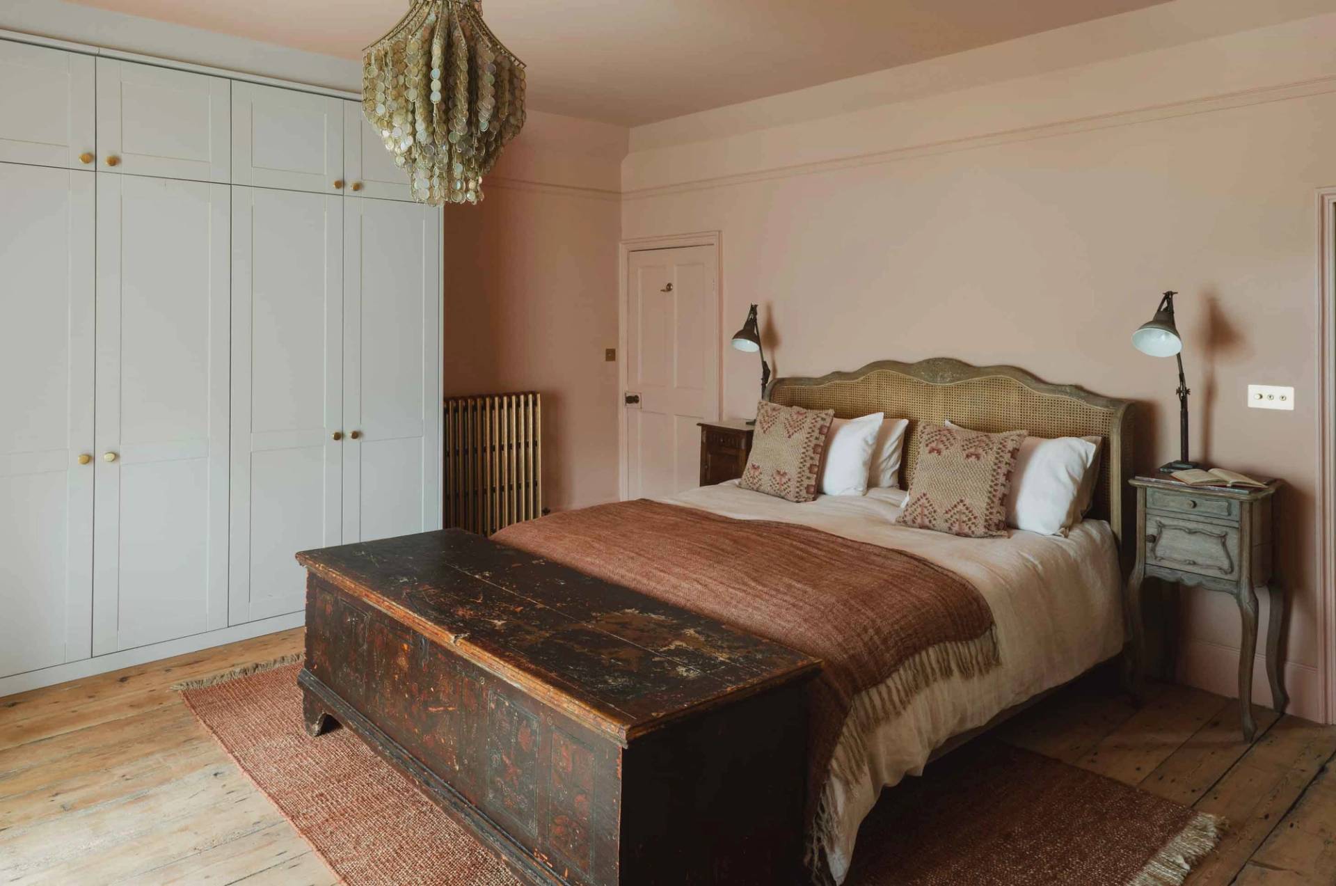 Soft pink bedroom shoot space with a cane headboard, dark wood trunk, and green chandelier in Newquay Cornwall TR8 by Love Locations.