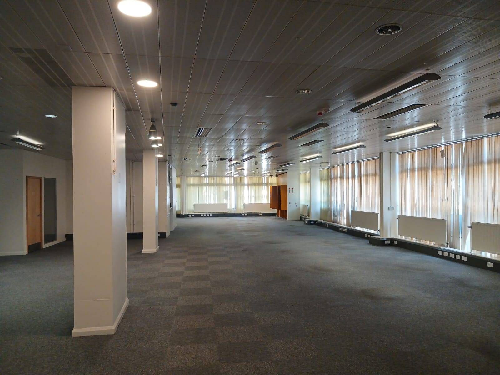 Moody, abandoned office interior shoot location in Watford WD18 from Love Locations, featuring a dark checkerboard carpet, grid ceiling tiles, and stark industrial lighting.