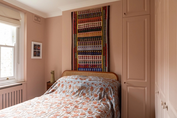 Earthy pink-toned bedroom location in Westminster SW1V for commercial photography by Love Locations, showing a patterned wall hanging above the bed and a built-in wardrobe.