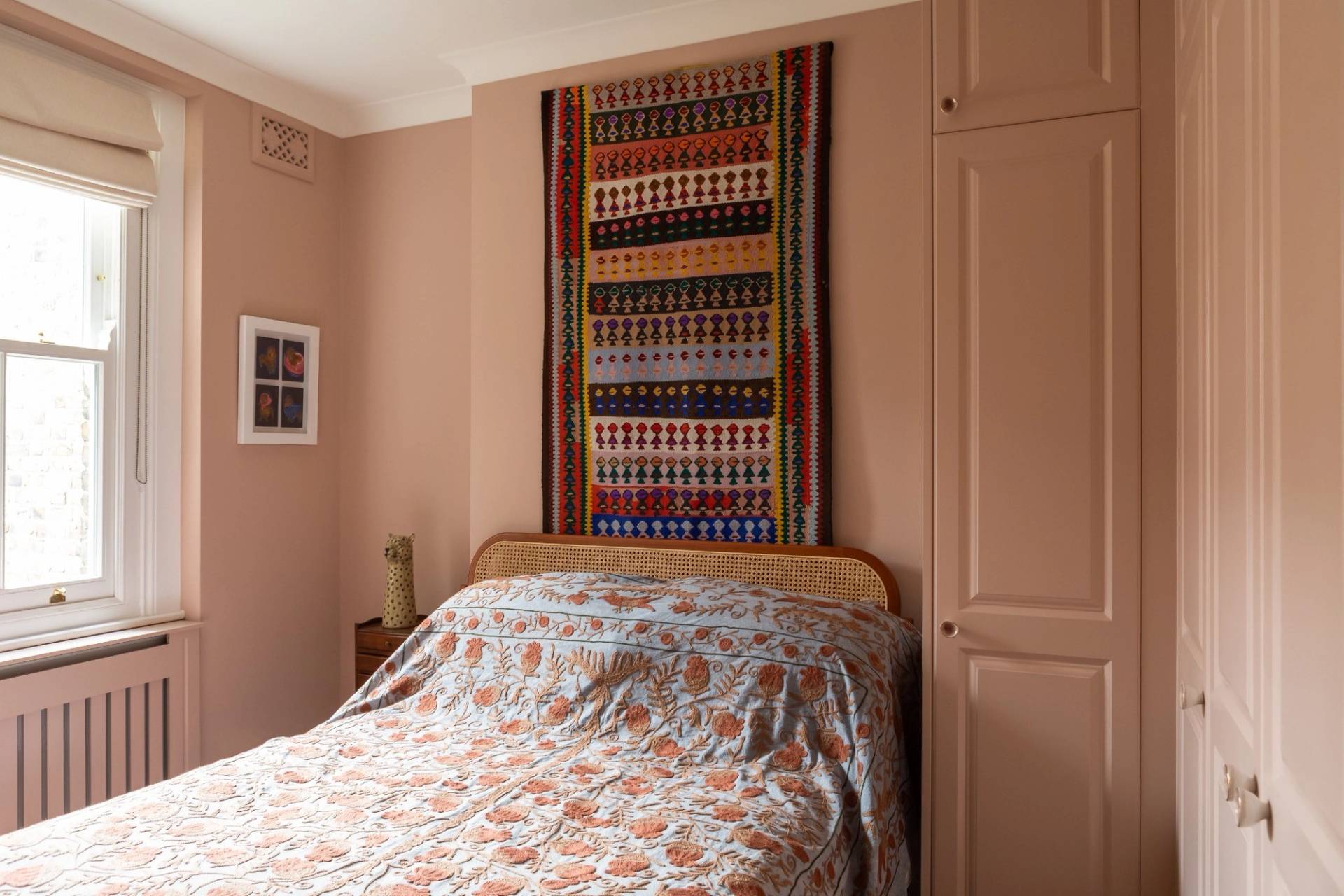 Earthy pink-toned bedroom location in Westminster SW1V for commercial photography by Love Locations, showing a patterned wall hanging above the bed and a built-in wardrobe.