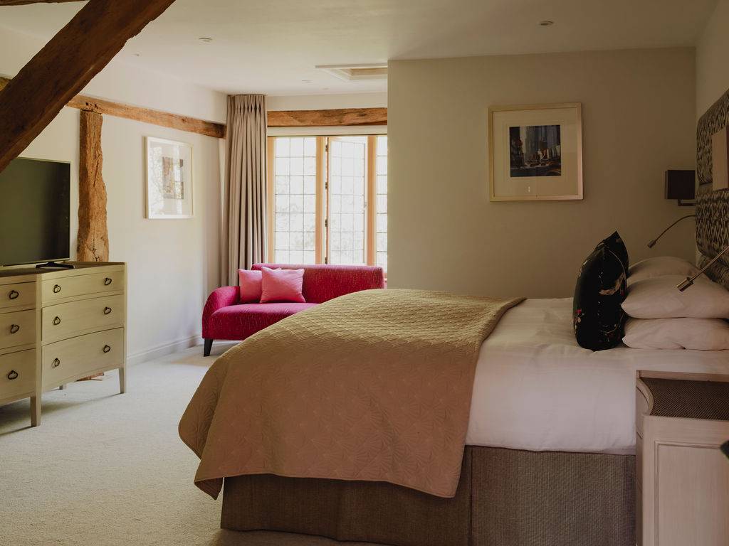 Spacious master bedroom location featuring a pink accent armchair, neutral bed linens, and leaded sash windows, Love Locations.
