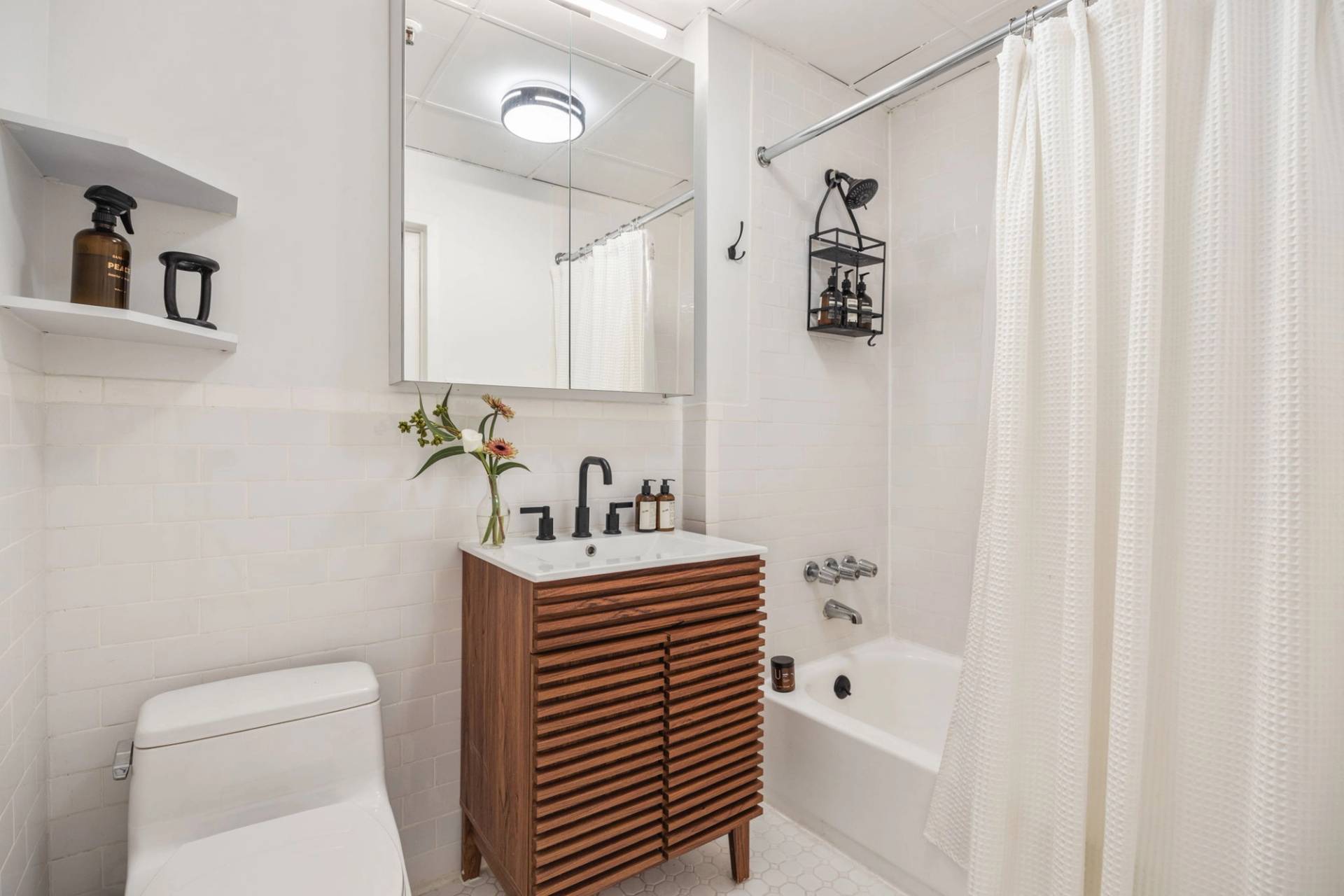  Clean white bathroom photoshoot space with a slatted wooden vanity, white bathtub, shower curtain, and overhead mirror in Tribeca 10007 by Love Locations.