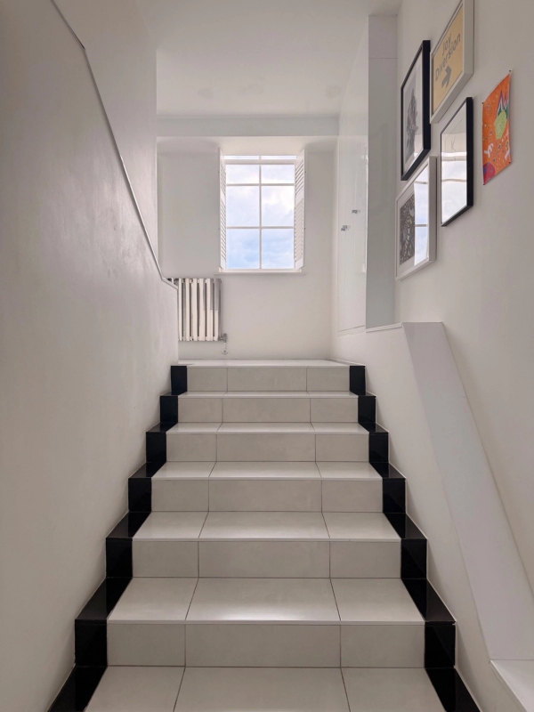 Clean minimalist white staircase corridor inside a converted school penthouse in Brixton SW4 via Love Locations, showing dark treads and bright natural lighting.