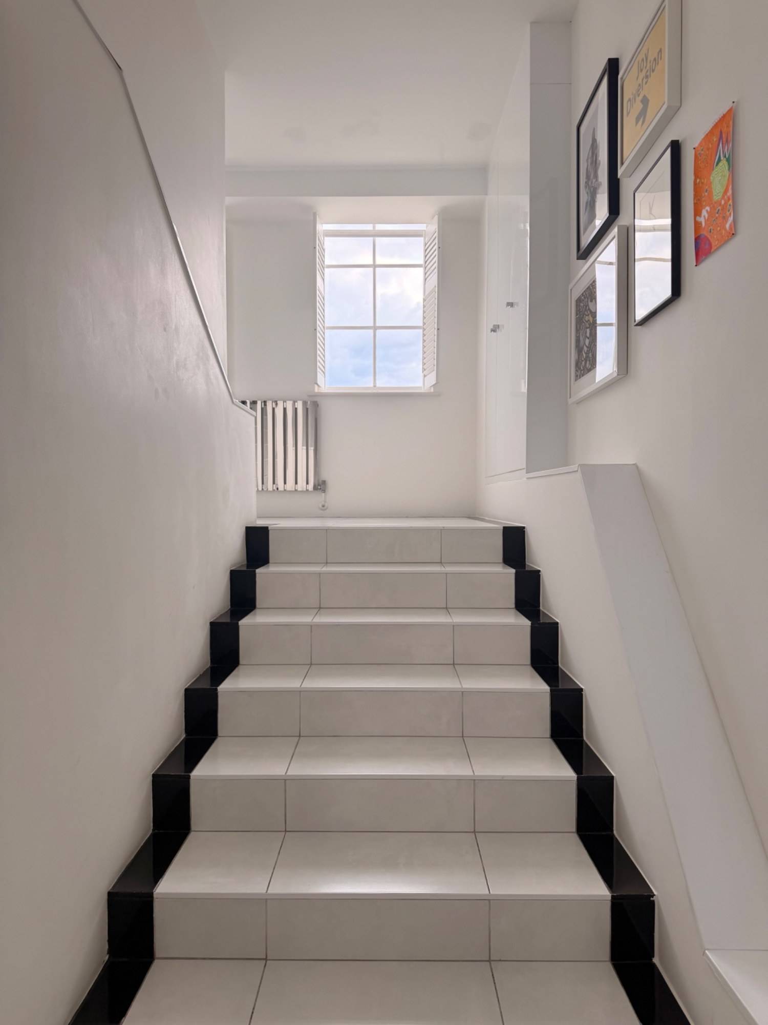 Clean minimalist white staircase corridor inside a converted school penthouse in Brixton SW4 via Love Locations, showing dark treads and bright natural lighting.