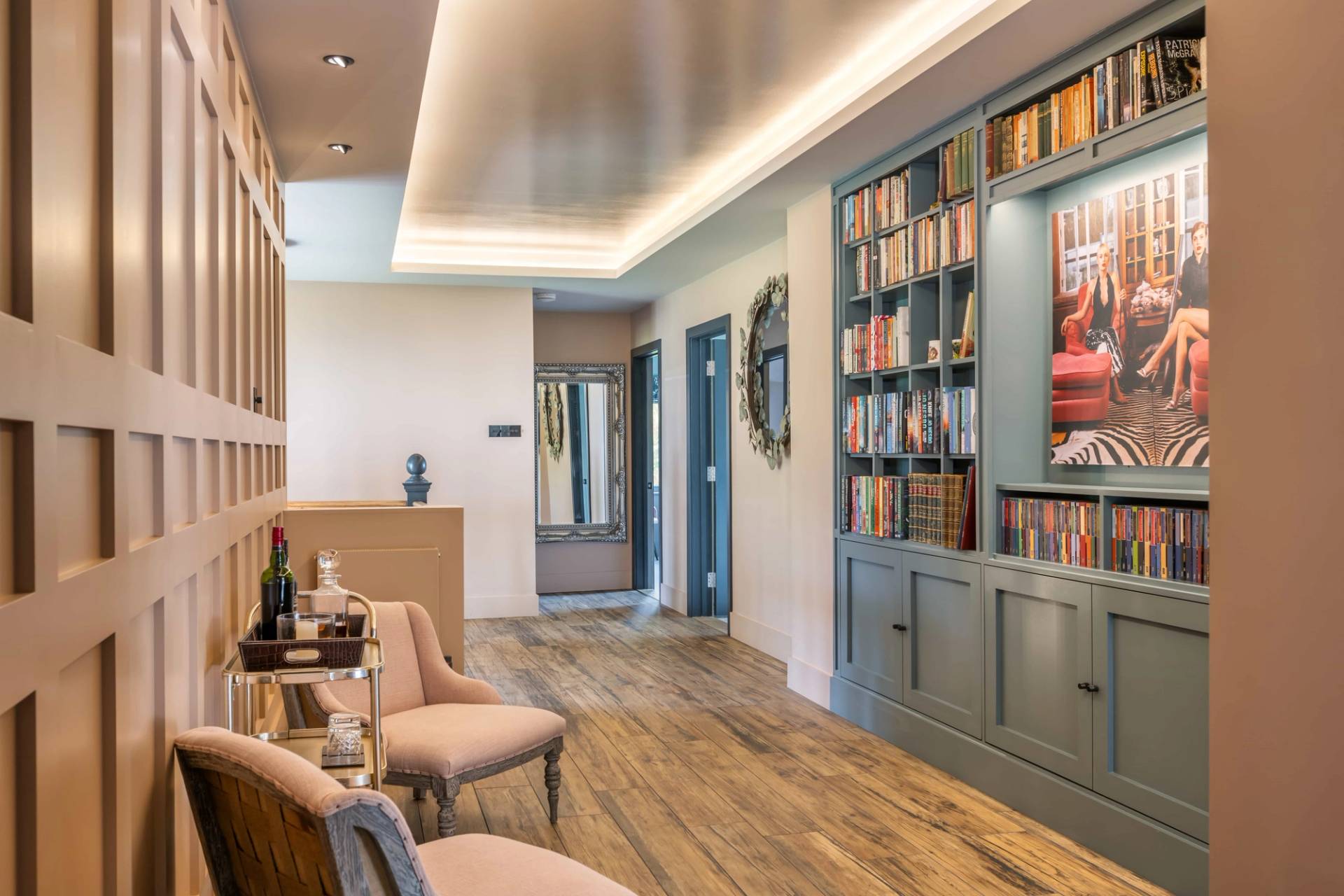 Upper floor reading lounge or study hall featuring built-in blue bookcases, oak flooring, and armchairs, Love Locations.