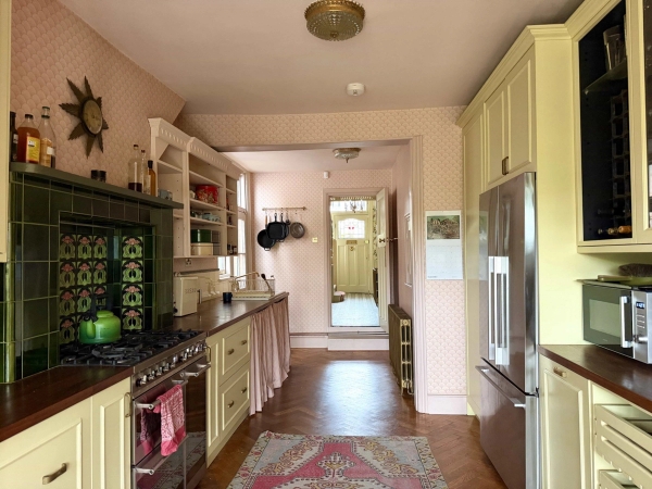 Wide perspective looking down a bright kitchen hallway towards a stained glass garden entrance, Love Locations N13.