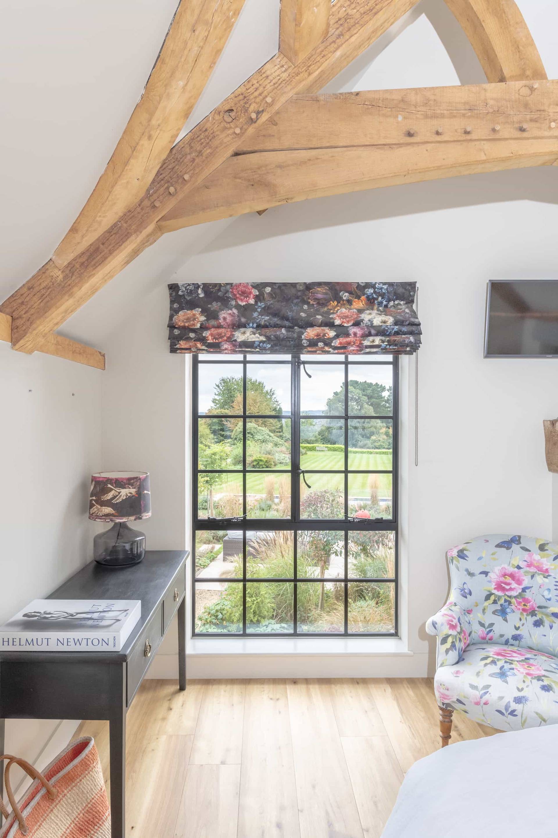 Sash window view framing stone barn walls set in a bedroom with floral blind, Love Locations GU28.