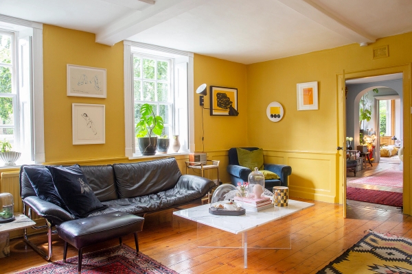 Lounge room with yellow painted wall panelling, black leather sofa, and glass coffee table, Love Locations ME13.