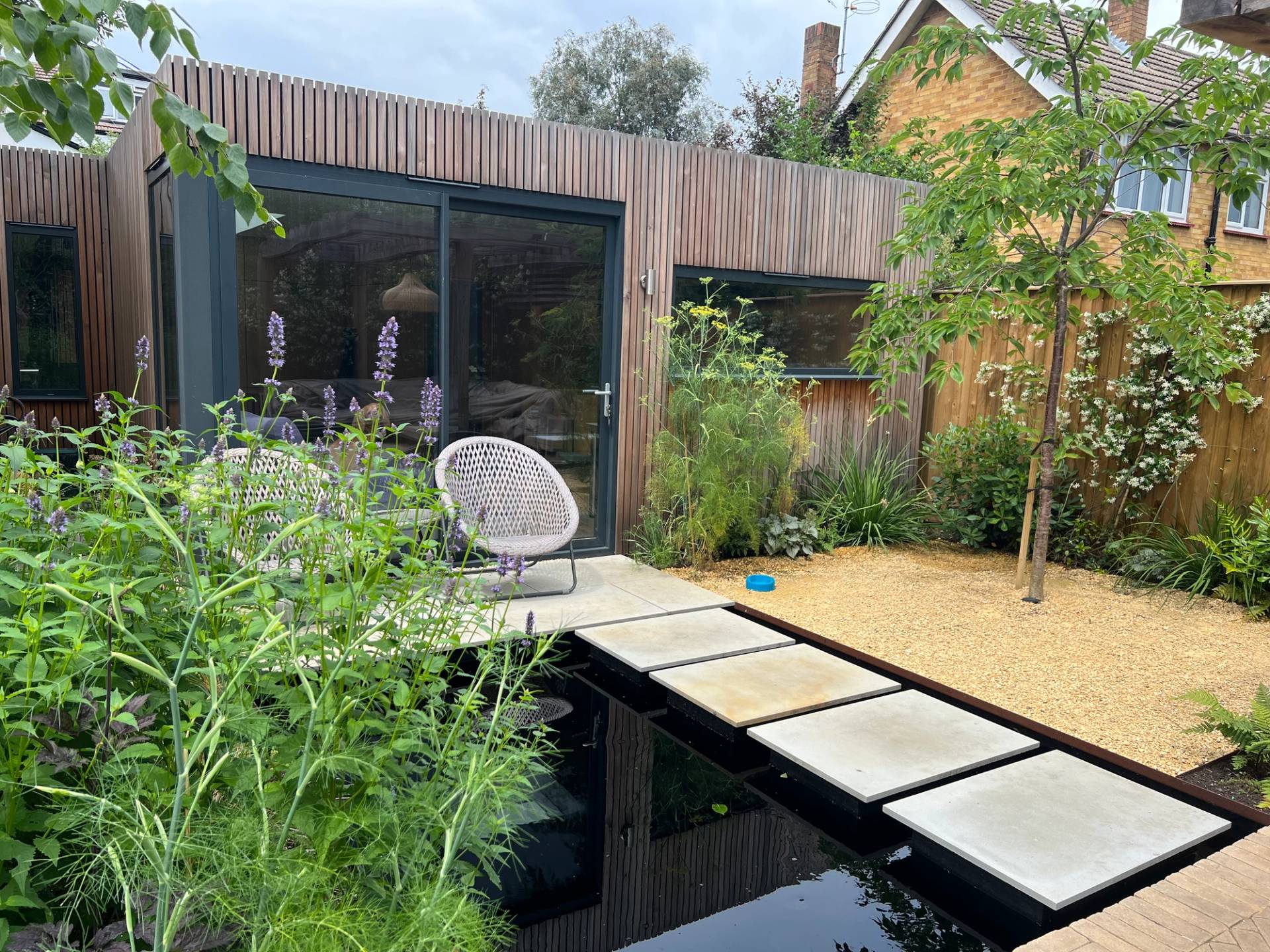 Garden stepping stone path crossing over a dark natural water pond toward a timber garden studio, Love Locations TW1.