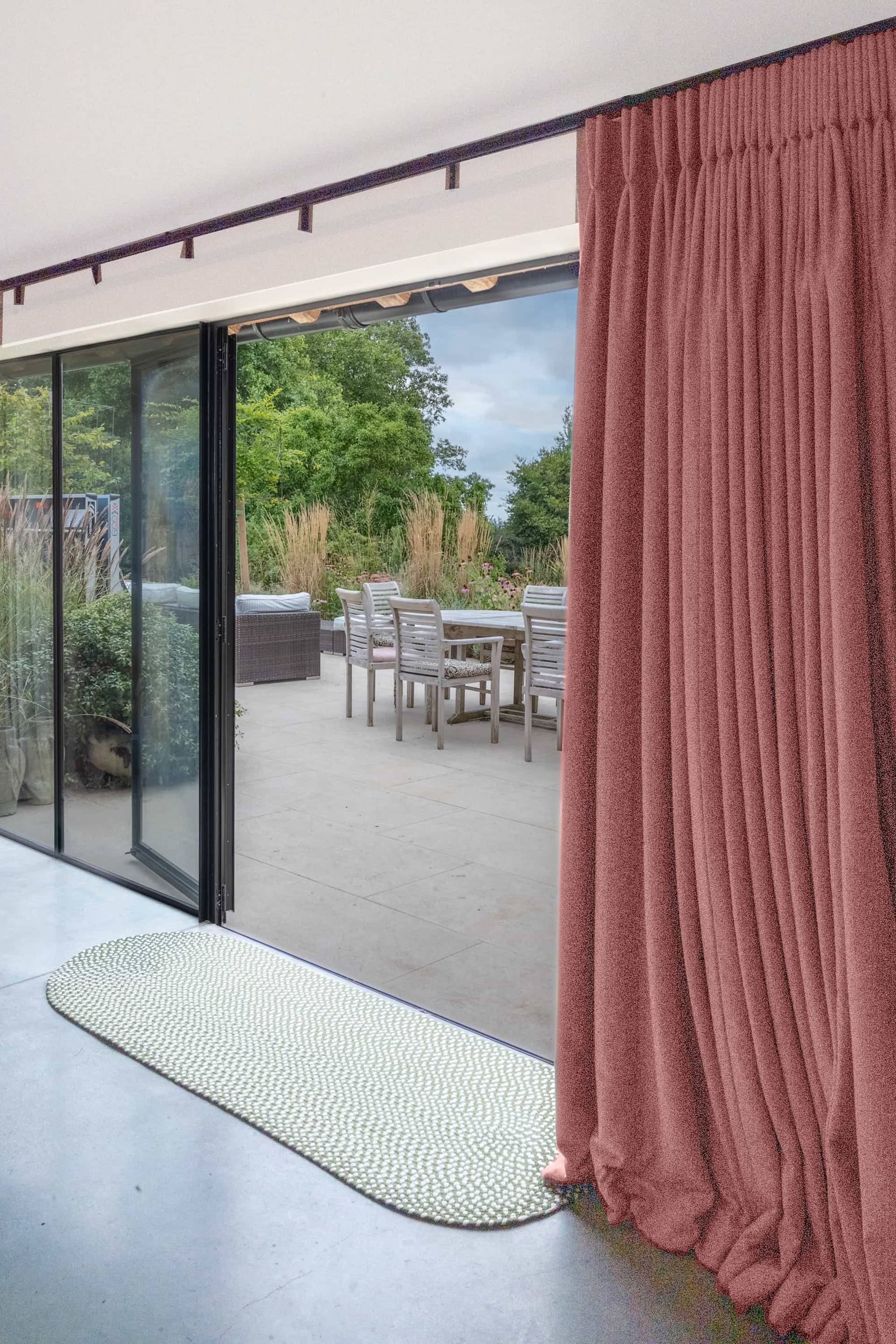 Open sliding glass doors with dark pink drapes looking out onto an outdoor paved dining terrace, Love Locations GU28.