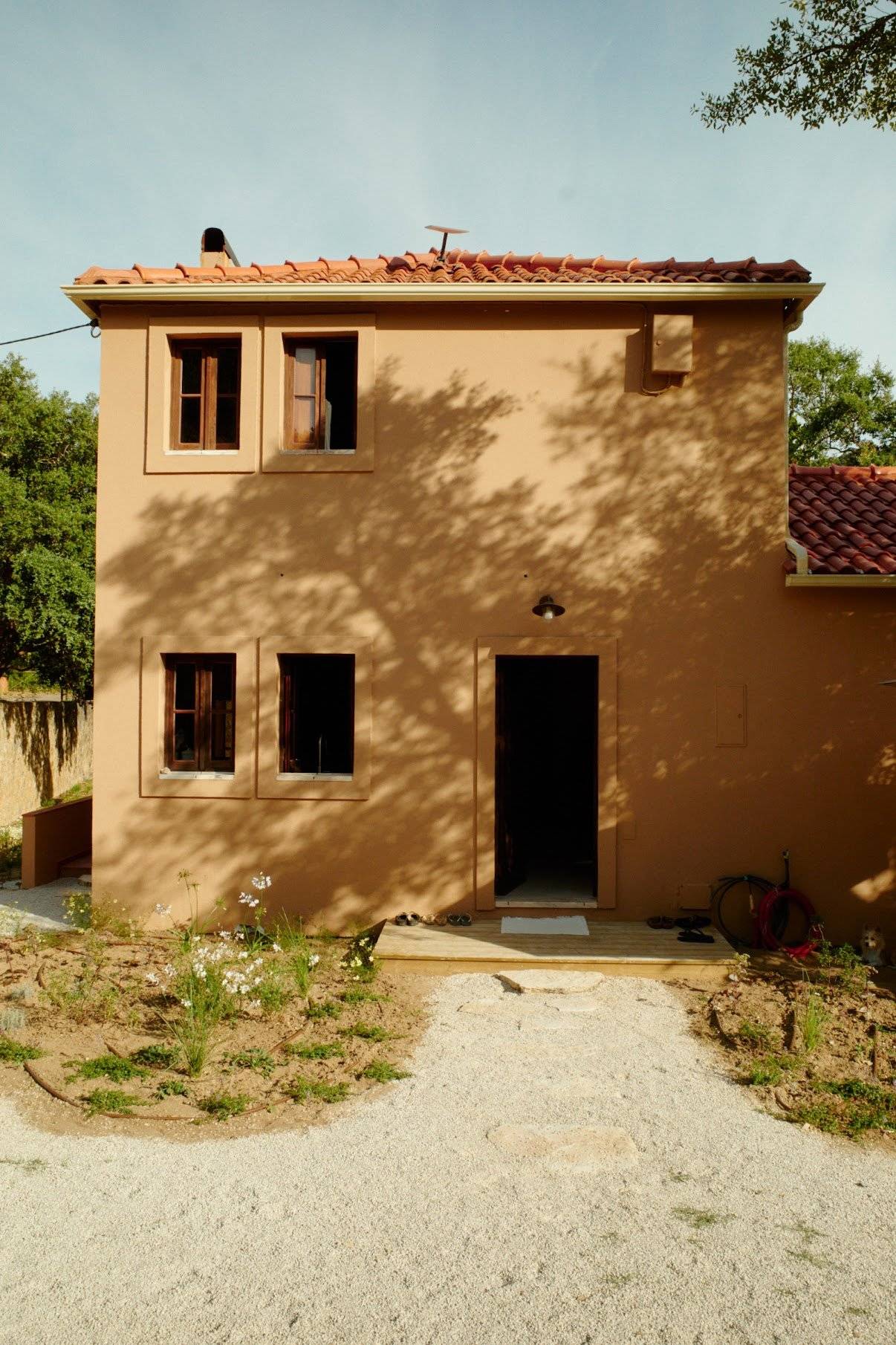 Warm terracotta plaster villa facade featuring wooden shuttered windows and gravel pathway, Love Locations 2705-064.