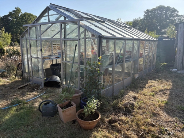 Industrial farm glasshouse exterior surrounded by terracotta plant pots and rural land, Love Locations BN8.